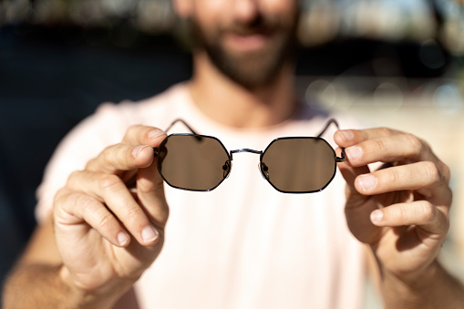 Closeup of man hands holding stylish sunglasses, selective focus. Summer, sun protection concept