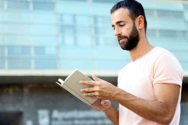 istock Pensive bearded man reading book standing on the street 1675780673