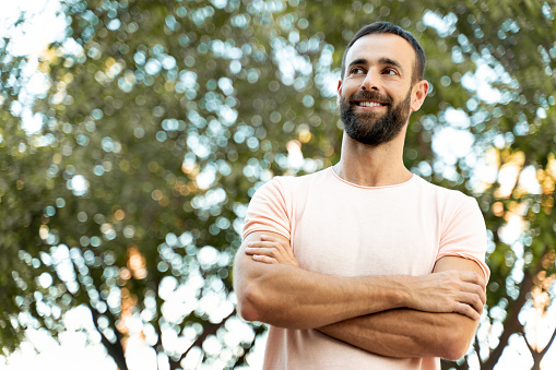 Handsome smiling latin man with arms crossed wearing casual clothing looking away standing in park