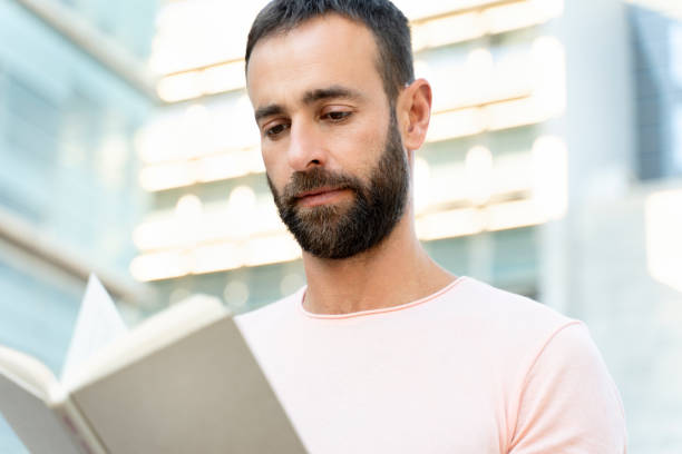 istock Handsome bearded middle aged man reading book, planning project on the street 1675780698