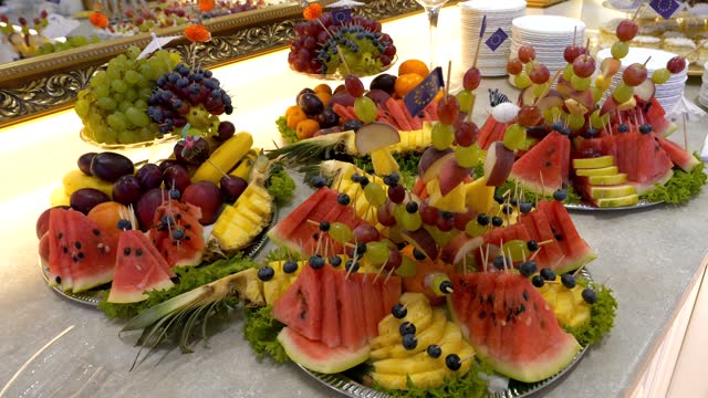 A table with fruits, platters of pineapple, watermelon, bananas, melon, and grapes
