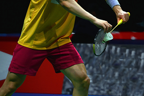 Male badminton player just about to making a serve while holding a white shuttlecock  on an indoor badminton court.