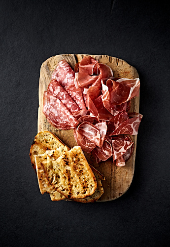 Italian Parma Ham, Coppa and Salami with bread toasts on wooden chopping board. Traditional antipasto. Top view
