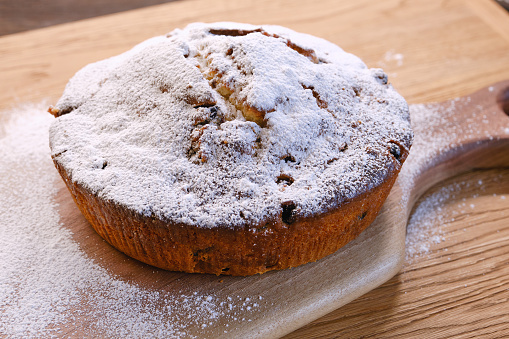 Fresh perfect bundt cake or muffin cake decorated icing sugar with raisins on a wooden table and board. Flat lay