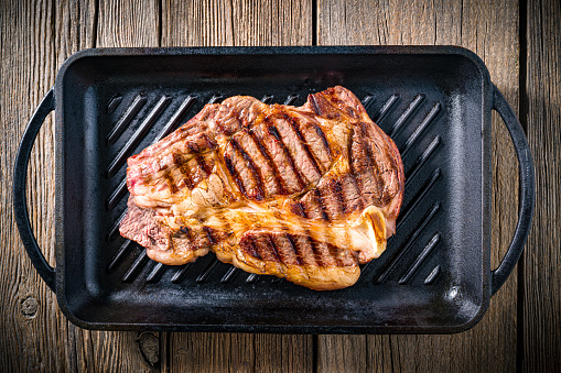 Beef rib steak grilled on a cast iron grill background on rustic dark wood table, top view flatlay