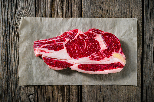 Beef rib steak raw on a butcher paper at supermarket on a rustic dark wood table background  top view flatlay
