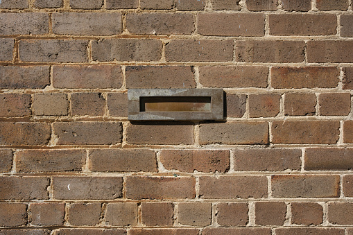 Old brass mail slot in a brick wall on a sunny morning.