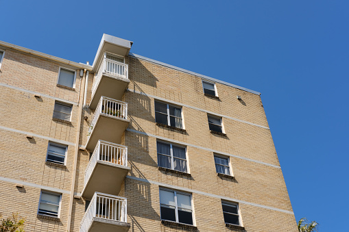 Low angle view of a brick building with large balconies against a blue sky.