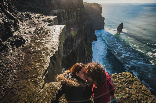Couple of male and female kidding on the edge of a high cliff. Man and woman kissing and loving on an adventure and romantic trip by the border of a tall cliff. Irish travel adventure concept - County Clare, Ireland