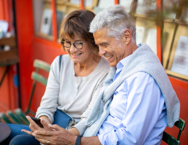 istock two smiling older people sitting outside looking at mobile phone 1675916130