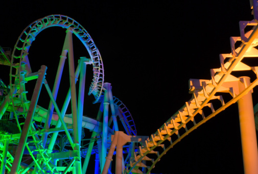 Modern rollercoaster lit up with different colors of light at night.