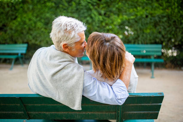 behind happy couple sitting on park bench kissing