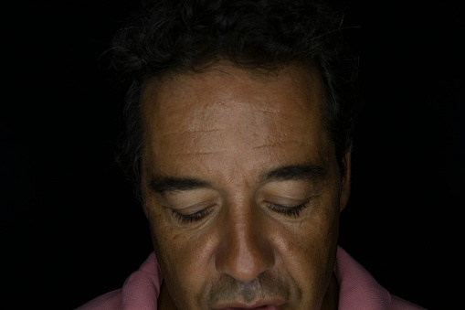 Portrait of a mature dark-haired man on a black background. Looking at the camera with ring of light reflected in the eyes