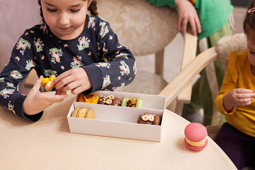 Three kids eat delicious tasty sweet color macarons.