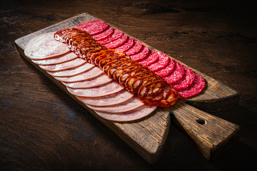 Cold cuts meat charcuterie slices in a row with pepperoni, chopped and sausage chorizo on a wooden cutting board on rustic table