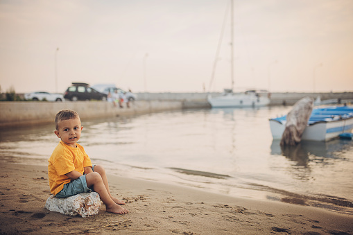Little boy sitting on the beach by the sea.