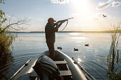 Waterfowl hunter in boat. hunter shooting to the flying duck at sunrise.