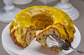 Сuted Panettone cake covered yellow chocolate glaze and drips on a white stand.