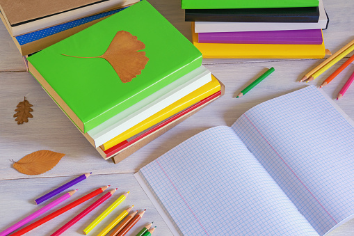 Autumn concepts. Stacks of different multicolored books, open notebook,  and colored pencils on rustic table. Copy space