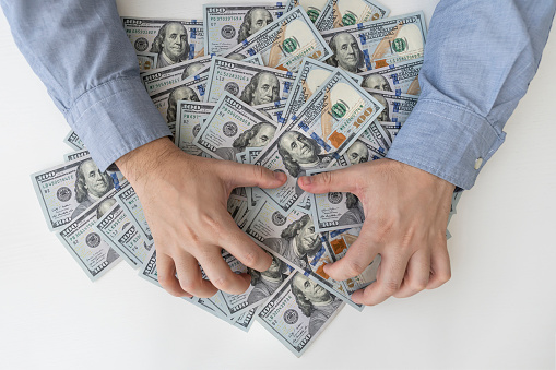 Man's hands and a lot of dollar bills on a white wooden table. Bribes, corrupt, cash. US dollars in male hands. The concept of profit, wages.