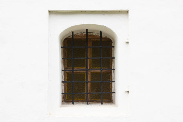 Old windows with bars in a white building. Small antique window.
