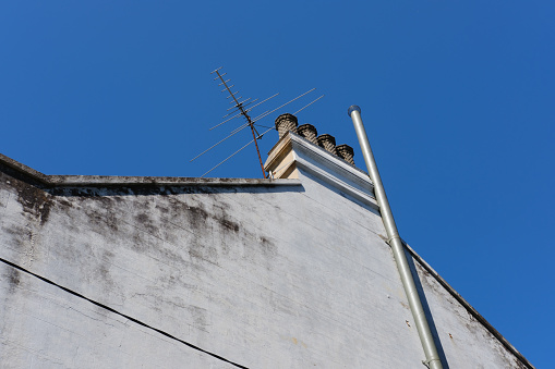 Close-up on a side wall of a building with chimney, antenna, and deep blue sky beyond.