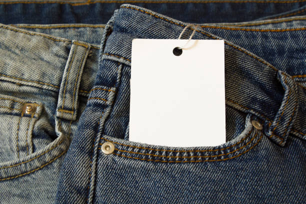 istock Label price tag mockup on blue jeans from white paper. 1675972083