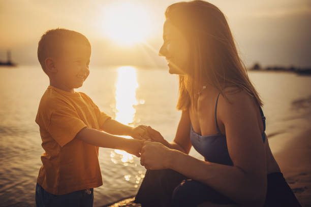 Woman with her little son on the beach by the sea in sunset, they are on vacation.