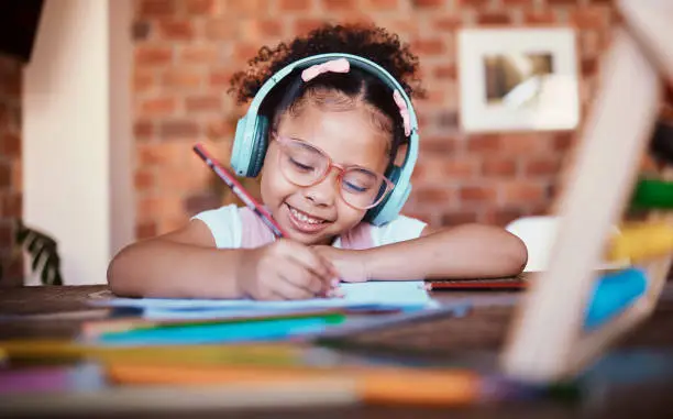 Photo of Writing, headphones and child at home with music, learning and homework for school. Kid, studying and happy with radio and audio streaming in a house with listening and drawing for creative project