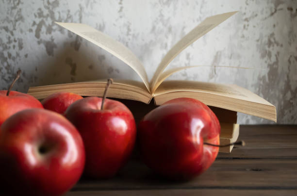 un libro abierto frente a una pared junto a manzanas rojas. las manzanas rojas brillantes y un libro abierto son un estilo antiguo. - book stack dieting textbook fotografías e imágenes de stock