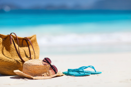 Straw hat, bag, sun glasses and flip flops on a tropical beach