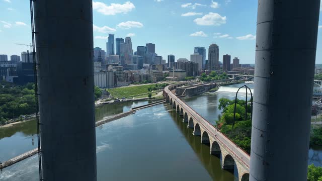 Reveal of Minneapolis, MN skyline from between smokestacks of University of Minnesota Southeast Steamplant. Aerial between metal pipes. View of downtown skyline and Stone Arch Bridge on waterfront.