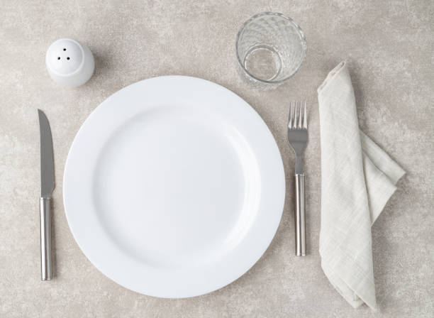 istock White empty ceramic plate with fork and knife, glass, salt and napkin over stone background 1675996569
