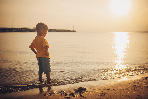 Little boy standing on the beach by the sea.