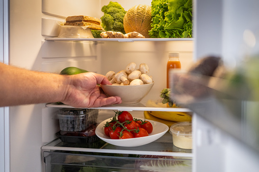 Man's hand taking out mushroom bowl from refrigerator at home.