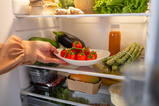 Woman's hand taking out tomato plate from refrigerator at home.