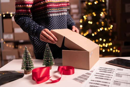 Woman online store small business owner seller packing package post shipping box on Christmas Eve. Ecommerce dropshipping. Close-up