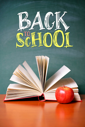 Chalkboard with BACK TO SCHOOL lettering. An apple with an open book on the desk. Space for copy.