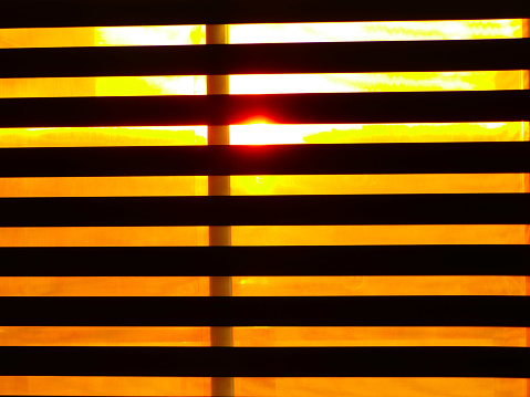 Orange light from early sunset peaking through open blinds