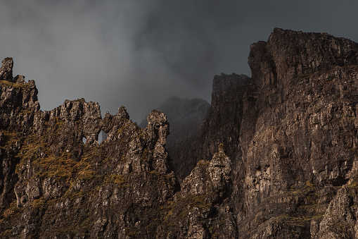 A misty, atmospheric, rocky landscape with golden sunrise light at the iconic rock pinnacle Old Man of Storr on the Isle of Skye in the Scottish Highlands.
