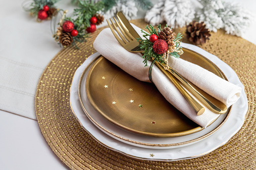 Pinecones festive place setting napkin decoration for dinner; glamorous holiday gold table centerpiece; cutlery on plate with Christmas artificial arrangement