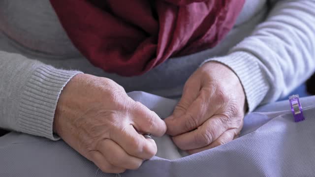 Close-up of a elderly woman sews by hand with a needle and thread. Selective focus.