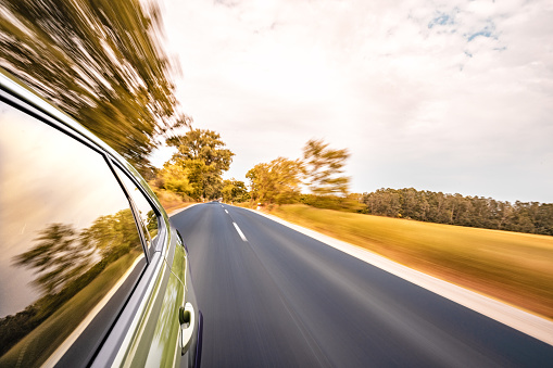 In the summertime, under the sunny sky, a car drives along the highway, creating a mesmerizing motion blur effect. As it speeds ahead, the surrounding environment becomes a blur of colors and shapes. Trees pass by in a rural landscape, accentuating the sense of a long journey. This exhilarating travel experience captures the thrill of speed and the allure of the open road.