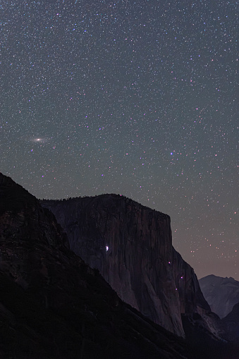 El Capitan of Yosemite Valley, silhouetted against the night sky. Seen in the frame are climbers spending the night on the cliff face and the Andromeda Galaxy above it.