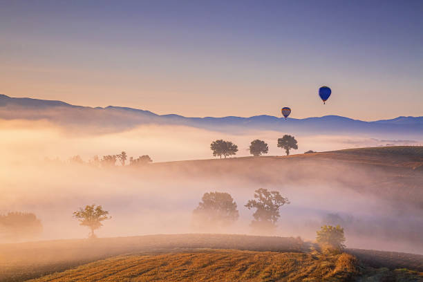 Hot air balloons flying over the foggy hills at sunrise