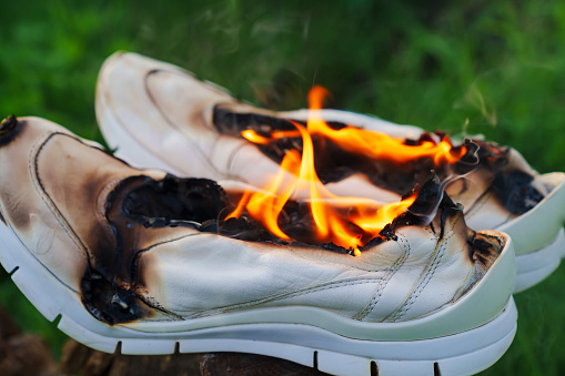 Burning white leather sports shoes. Sneakers or gym shoes on fire stand on the Stump in the meadow. athlete burned out in training. burnout from physical exertion, training