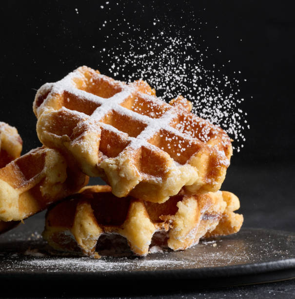 A stack of baked Belgian waffles sprinkled with powdered sugar