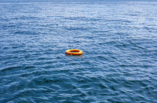 Orange life buoy floating in vast expanse of sea. Red lifebuoy float on ocean waves. Lifeguard equipment with rope swimming in lake. Concept of help, rescue, drowning, saving, surviving, protection