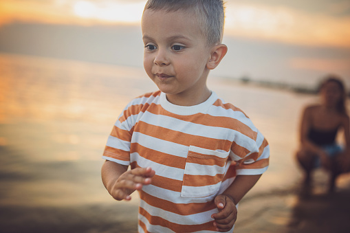 Woman with her little son on the beach by the sea, they are on vacation.