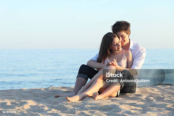 Couple Embracing Sitting On The Sand Stock Photo - Download Image Now - Boyfriend, Adolescence, Adult